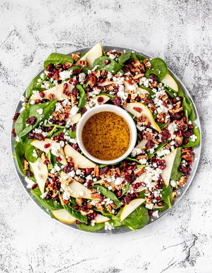 the christmas wreath salad with pomegranate pears and cranberries on a large platter with bowl of dressing in the centre