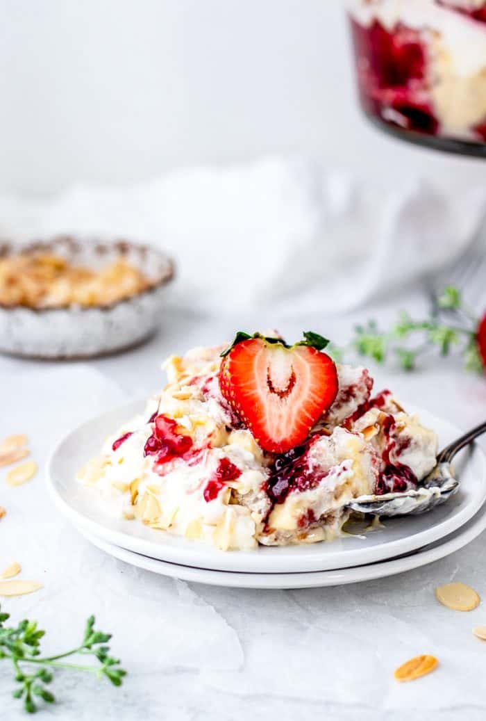 spoon on a white plate with a serving of trifle topped with a strawberry