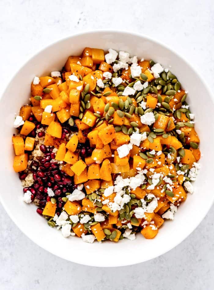 The squash, pomegranates, pumpkin seeds, quinoa and feta added to a big white bowl