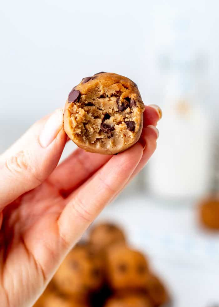 A hand holding a protein cookie dough ball with a bite taken out of it.
