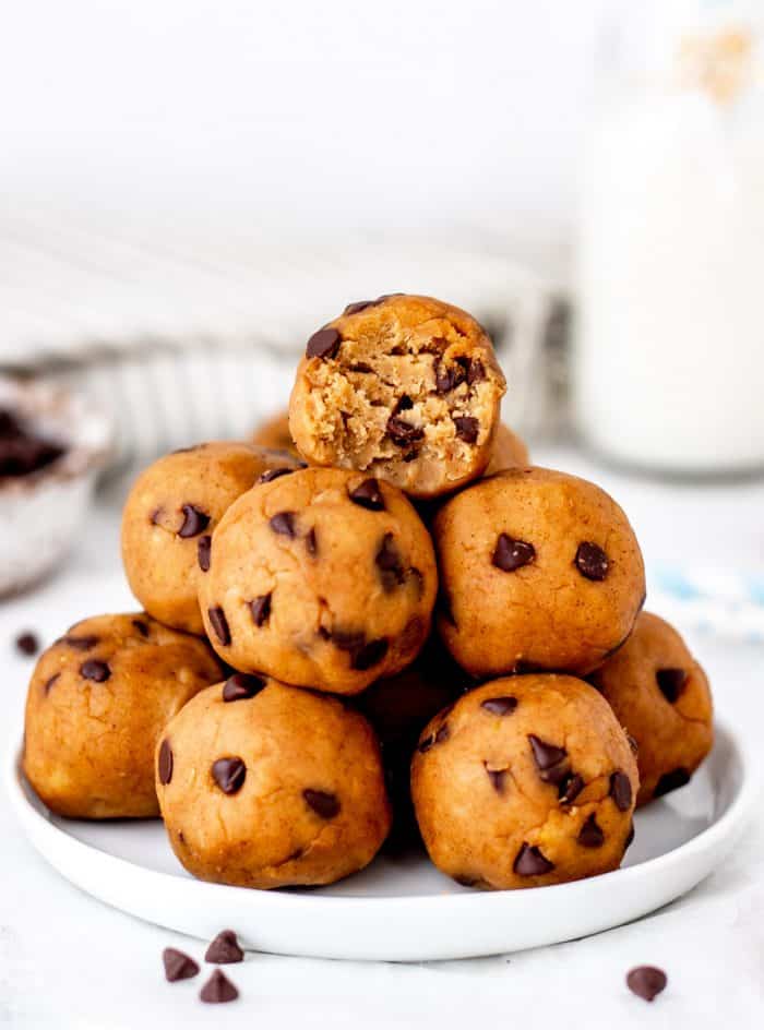 Chocolate chip cookie dough balls on a plate with a bite taken out of the top one.