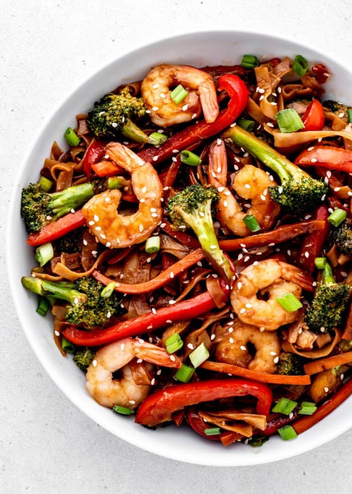 Overhead shot of shrimp noodle stir fry in a bowl with sesame seeds and green onion..