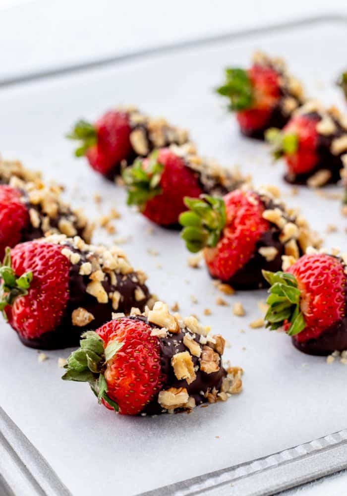 Dark chocolate dipped strawberries with walnuts on a baking sheet.