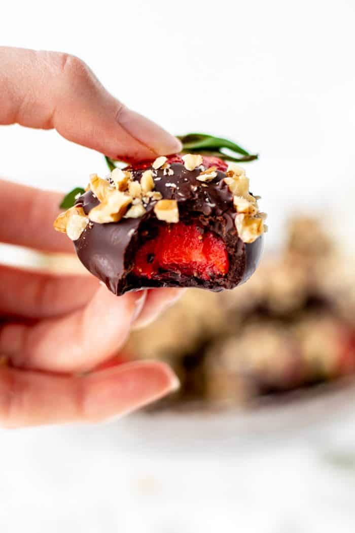 A hand holding a chocolate covered strawberry with a bite taken out of it.