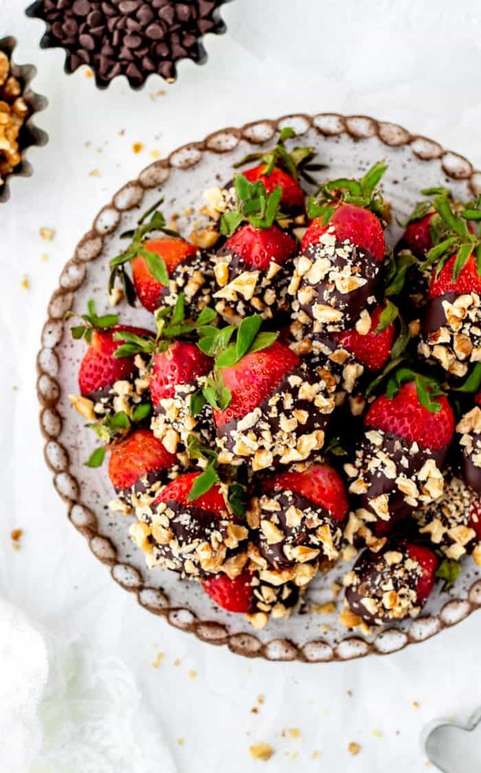 Overhead shot of chocolate and nut covered strawberries on a serving plate.