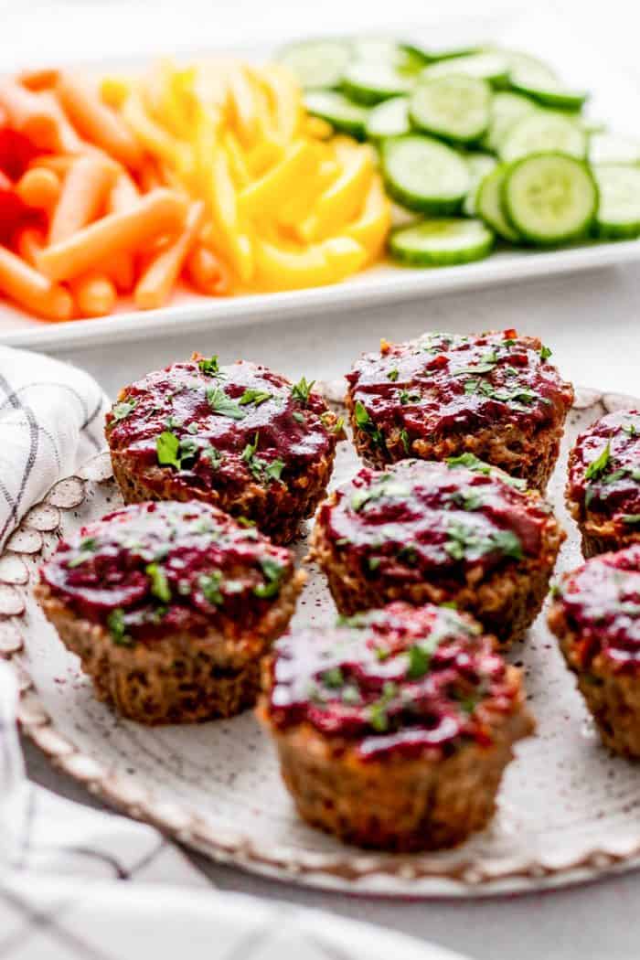 A plate of mini BBQ meatloaf muffins next to a plate of vegetables.