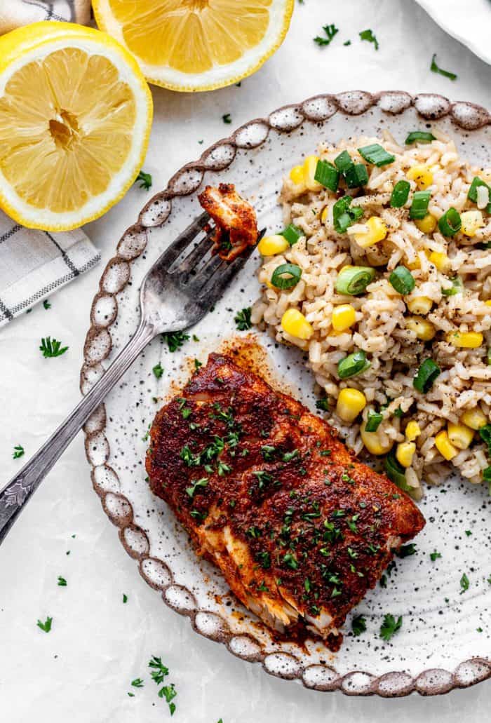 Blacked cod fillet on a plate with a side of brown rice and corn.