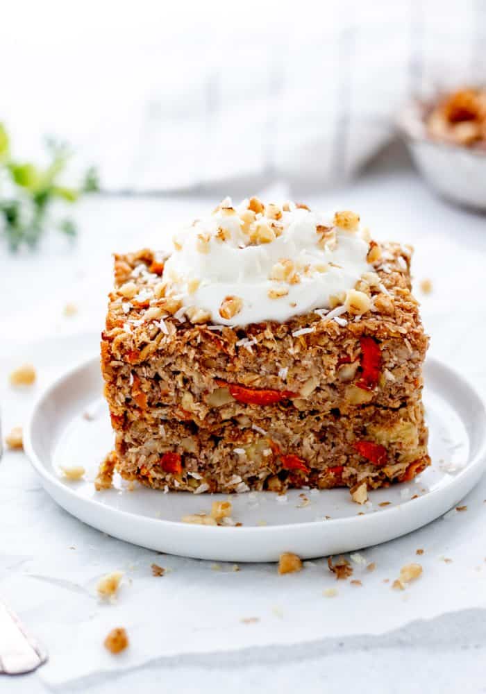 A piece of carrot cake baked oatmeal on a plate topped with yogurt and walnuts.