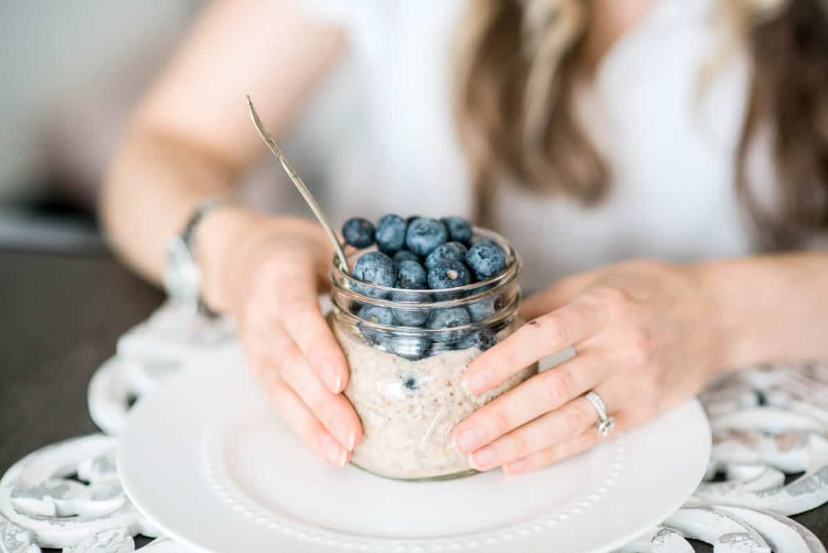 Hands holding a mason jar filled with protein overnight oats topped with blueberries.