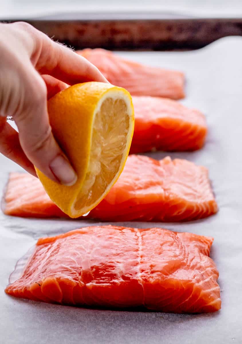 Lemon being squeezed over salmon.