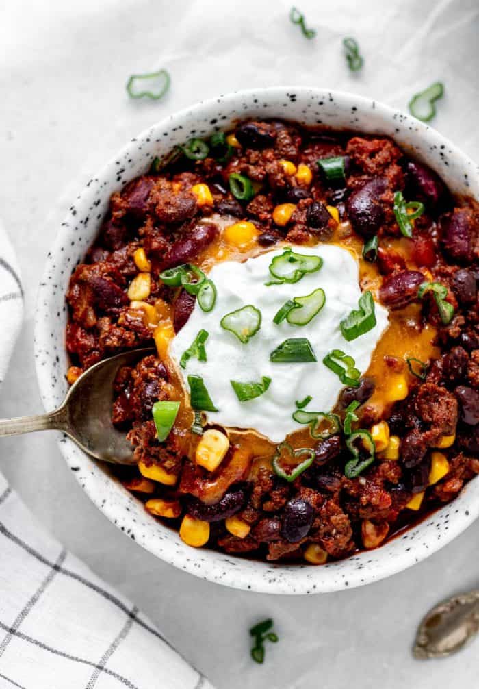 Overhead shot of spoon digging into a bowl of chili topped with cheese and yogurt.
