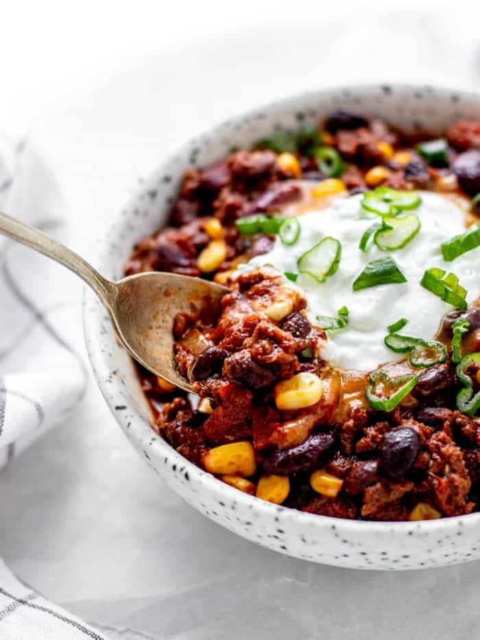 A spoon digging into a bowl of high protein chili with corn and beans.