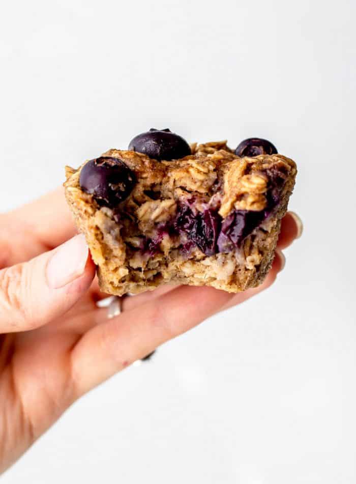 A hand holding a blueberry banana oatmeal muffin with bite taken out of it..
