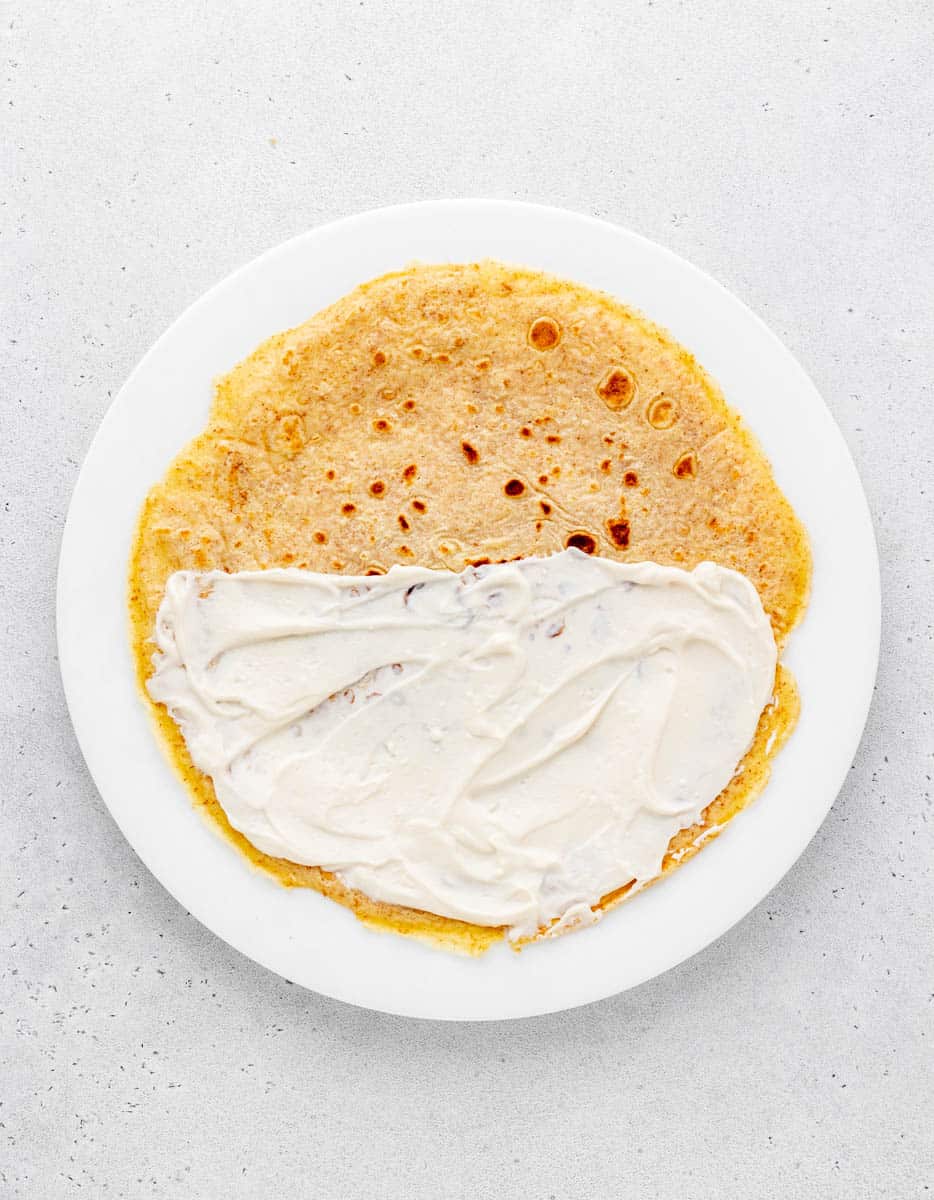 Cream cheese filling spread on half a crepe.