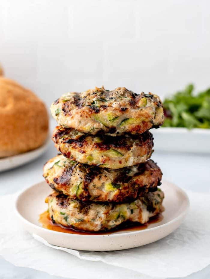 A stack of turkey burgers on a plate next to buns and arugula.