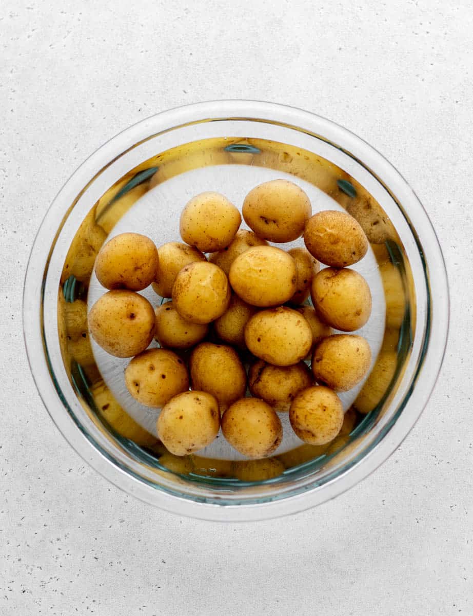 Cooked potatoes in cold water and being drained.