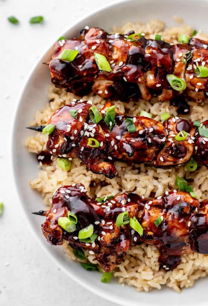 Three teriyaki chicken kabobs in a bowl on a bed of rice.
