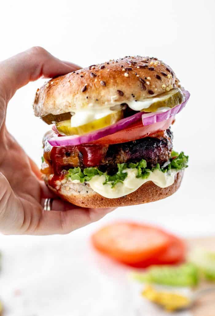 A hand holding a burger in a bun.