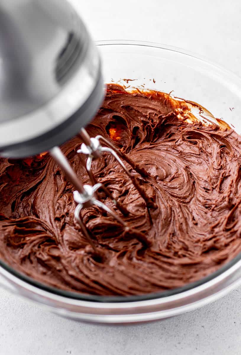 A hand mixer whipping the chocolate frosting.