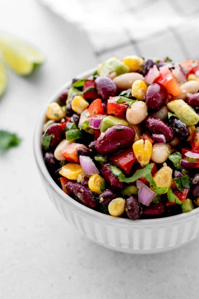 Bean salad with avocado in a small white bowl.