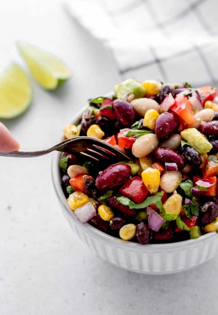 Vegetarian bean salad in a small white bowl with fork digging in.