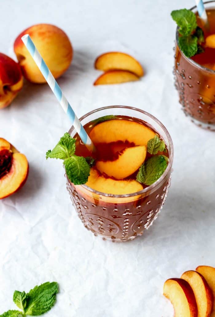 Overhead image of caffeine-free iced peach tea topped with peaches and mint with a straw.
