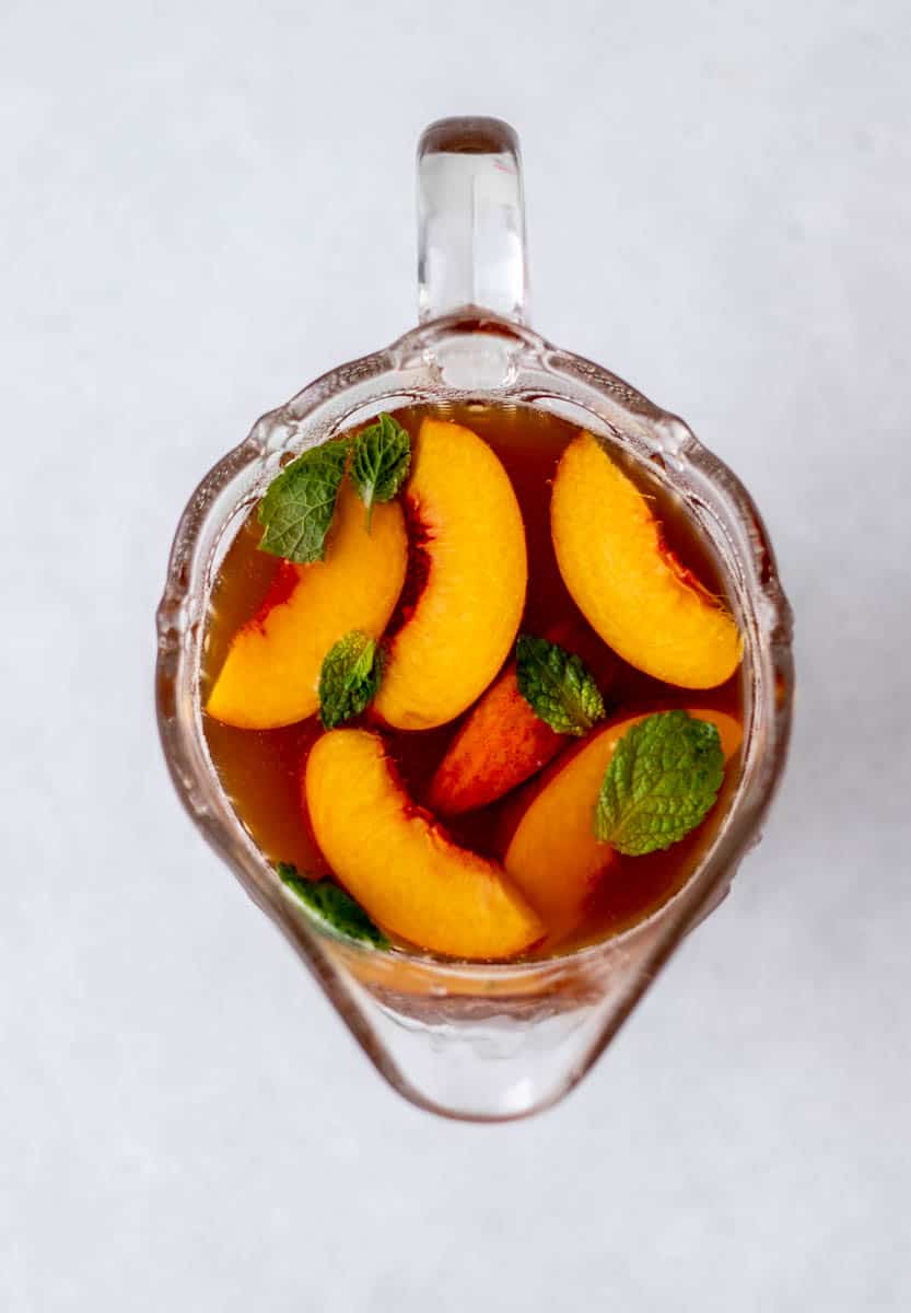 Overhead image of a glass pitcher full of decaf peach iced tea topped with peach slices and fresh mint leaves.