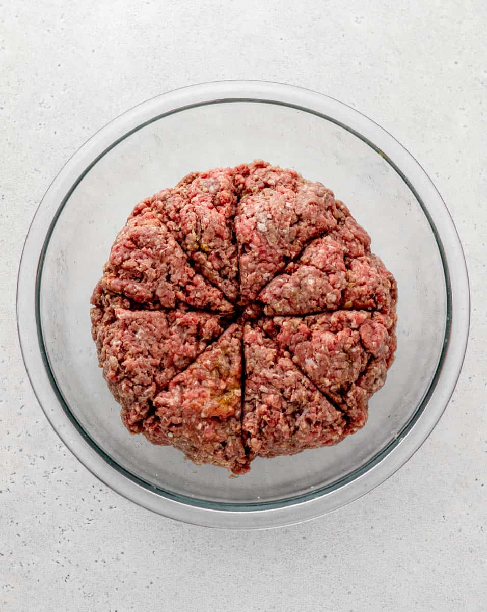 Raw burger mixture in a glass bowl sliced into 8 portions.