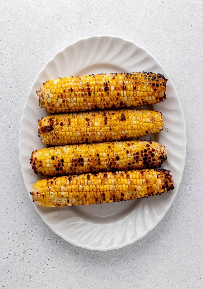 Charred corn on the cob on a white tray.