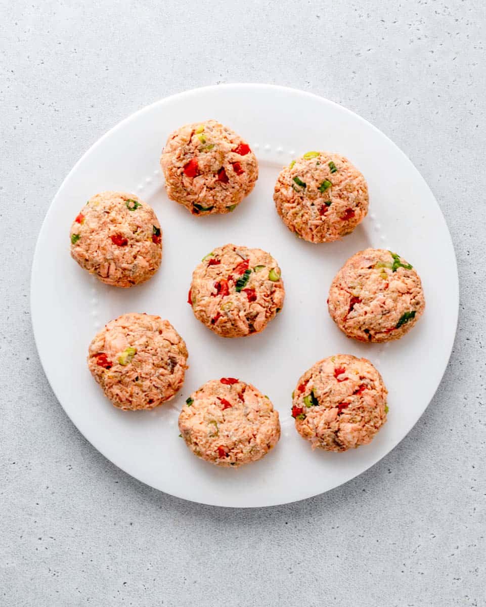 8 uncooked healthy salmon patties on a white plate.