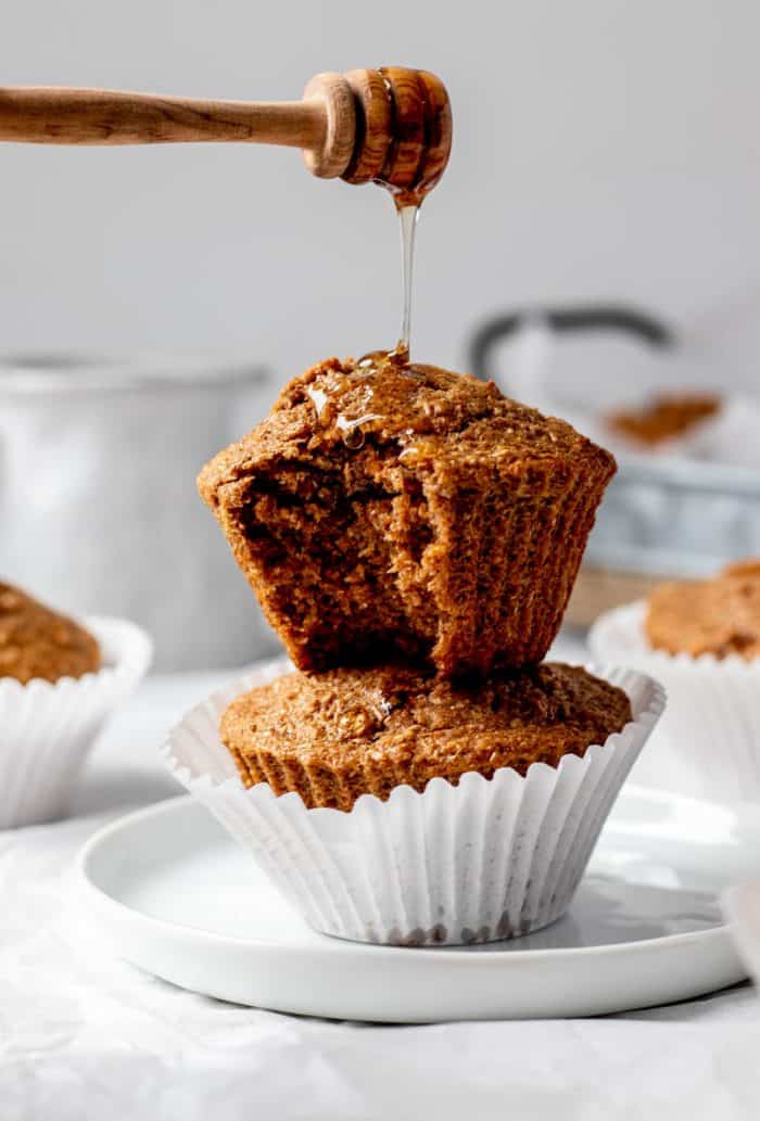 Two honey bran muffins stacked on top of each other and honey being drizzled over them.