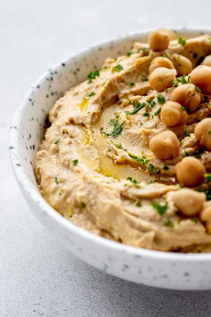 Up close shot of roasted garlic hummus on a bowl topped with chickpeas.