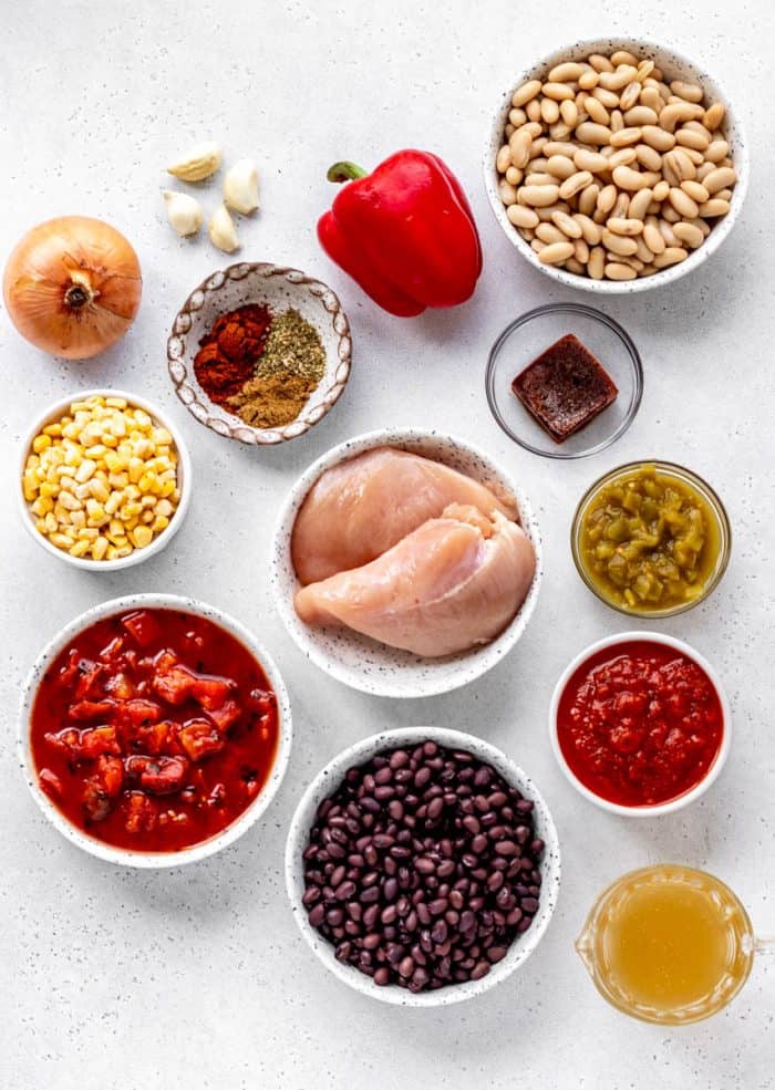 Overhead image of ingredient for slow cooker creamy chicken enchilada soup including chicken, pepper, onions, tomatoes, corn, beans, and spices.