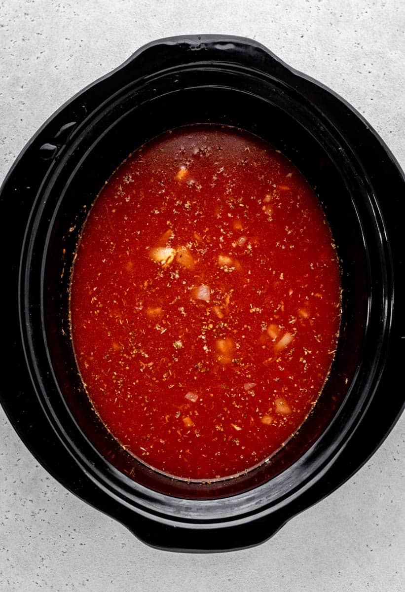 Overhead image of vegetables, broth and tomatoes in a slow cooker.