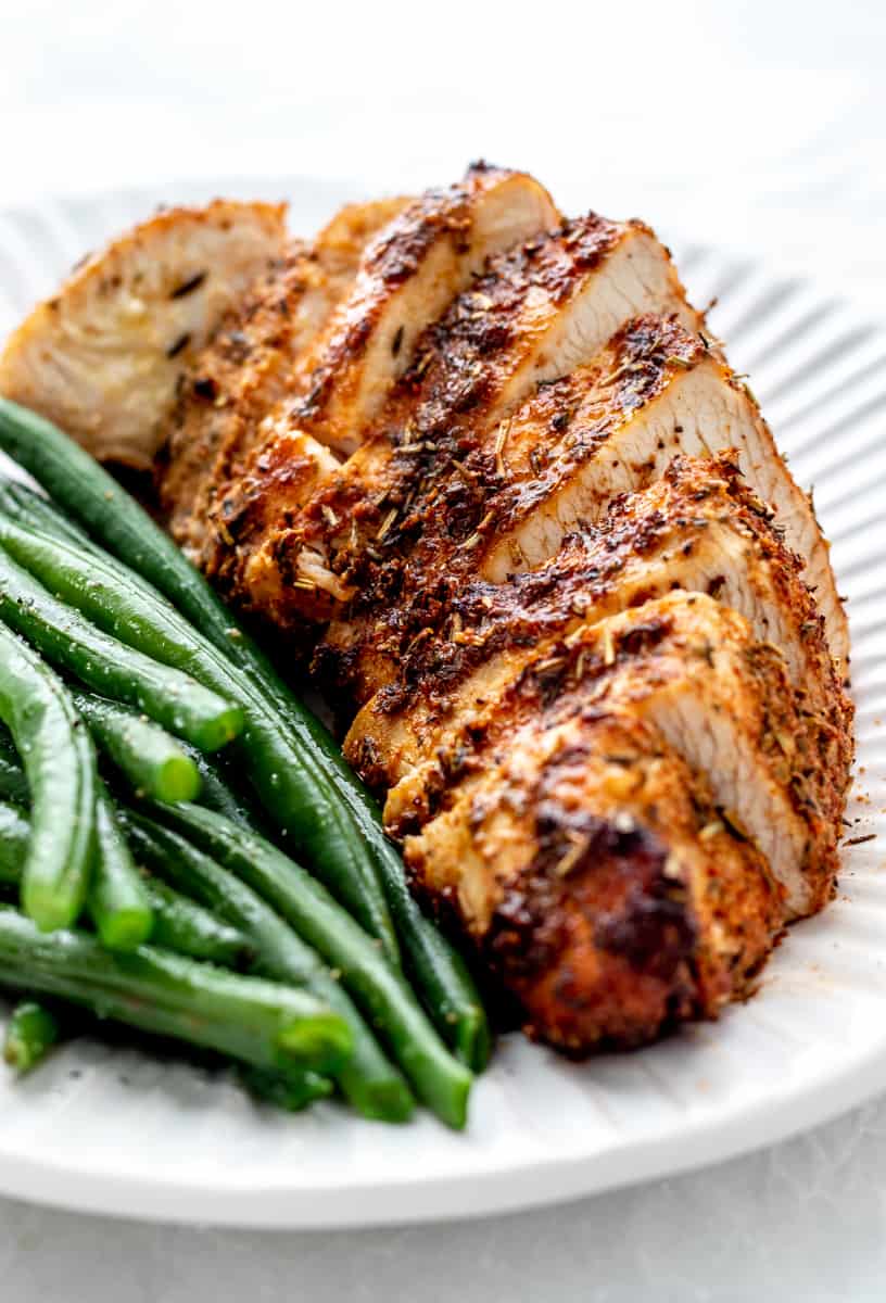 Sliced air fryer boneless turkey breast on a white plate with green beans.