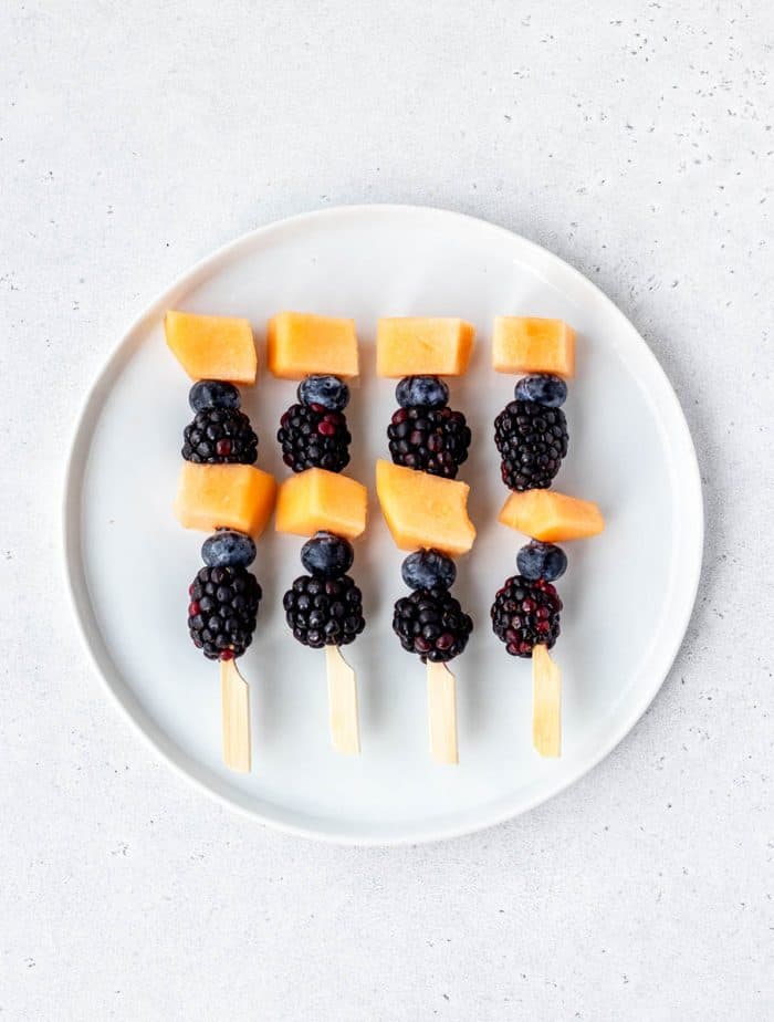 Halloween fruit kabobs on a white plate.