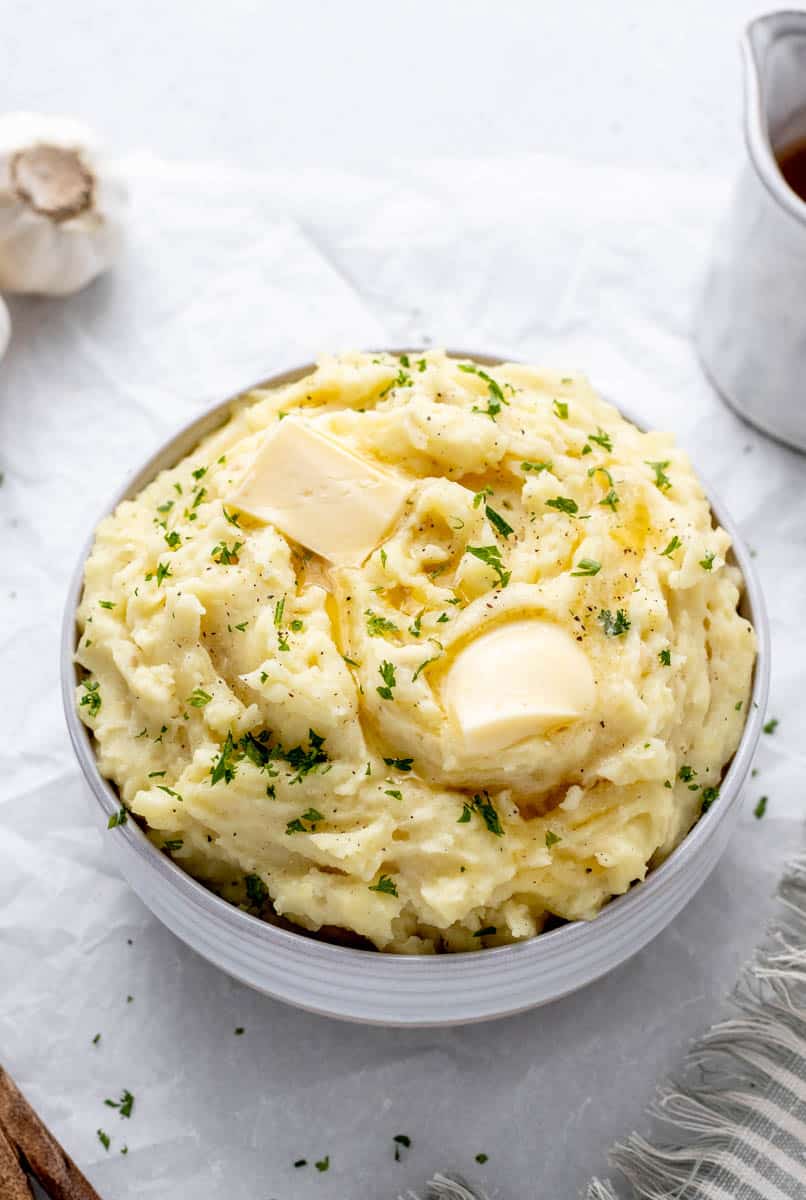 Greek yogurt mashed potatoes in a bowl topped with parsley and pats of butter.