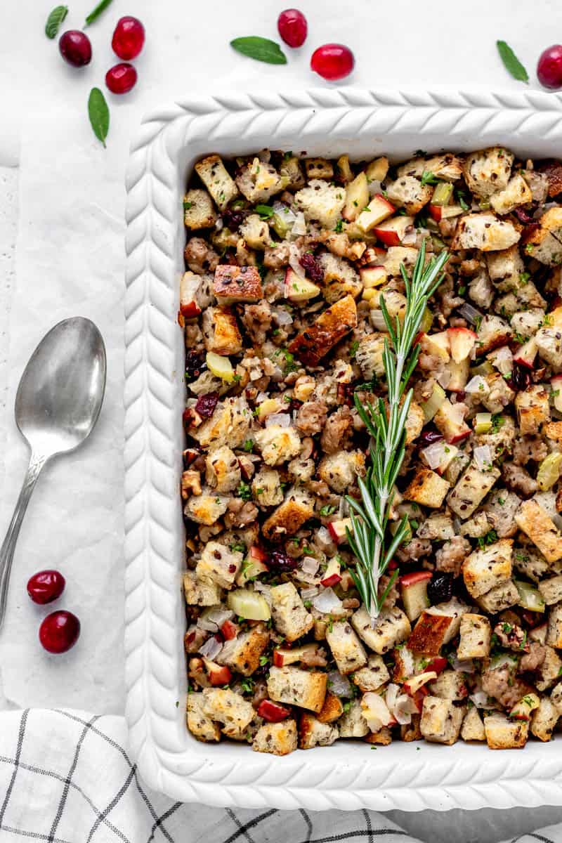 Close up overhead shot of sausage stuffing in white baking dish topped with fresh rosemary.