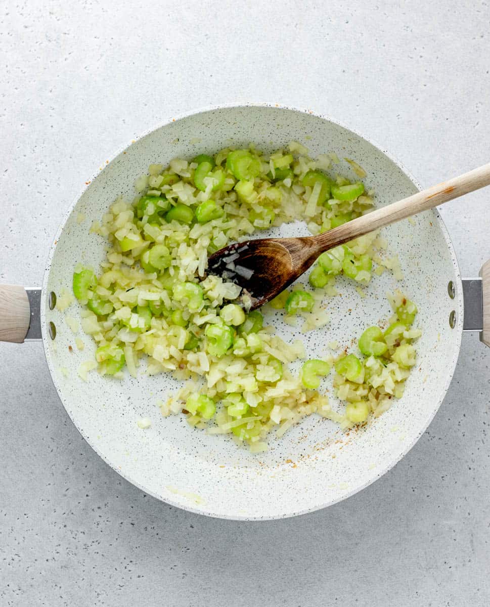 Onions and celery sautéeing n a large pot being stirred with a wooden spoon.