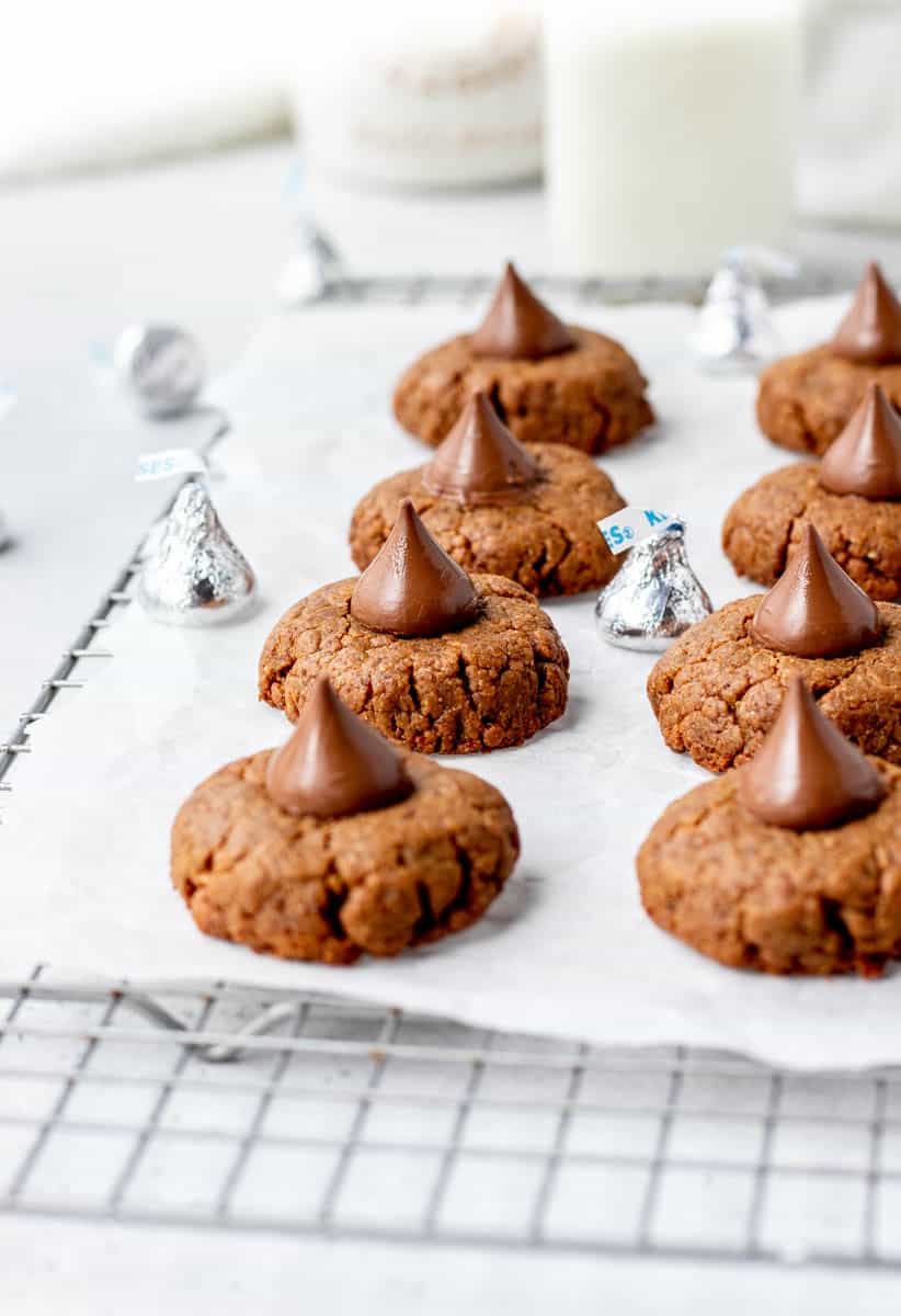 Peanut butter blossom cookies on a cooling rack with a few silver wrapped Hershey's kisses.