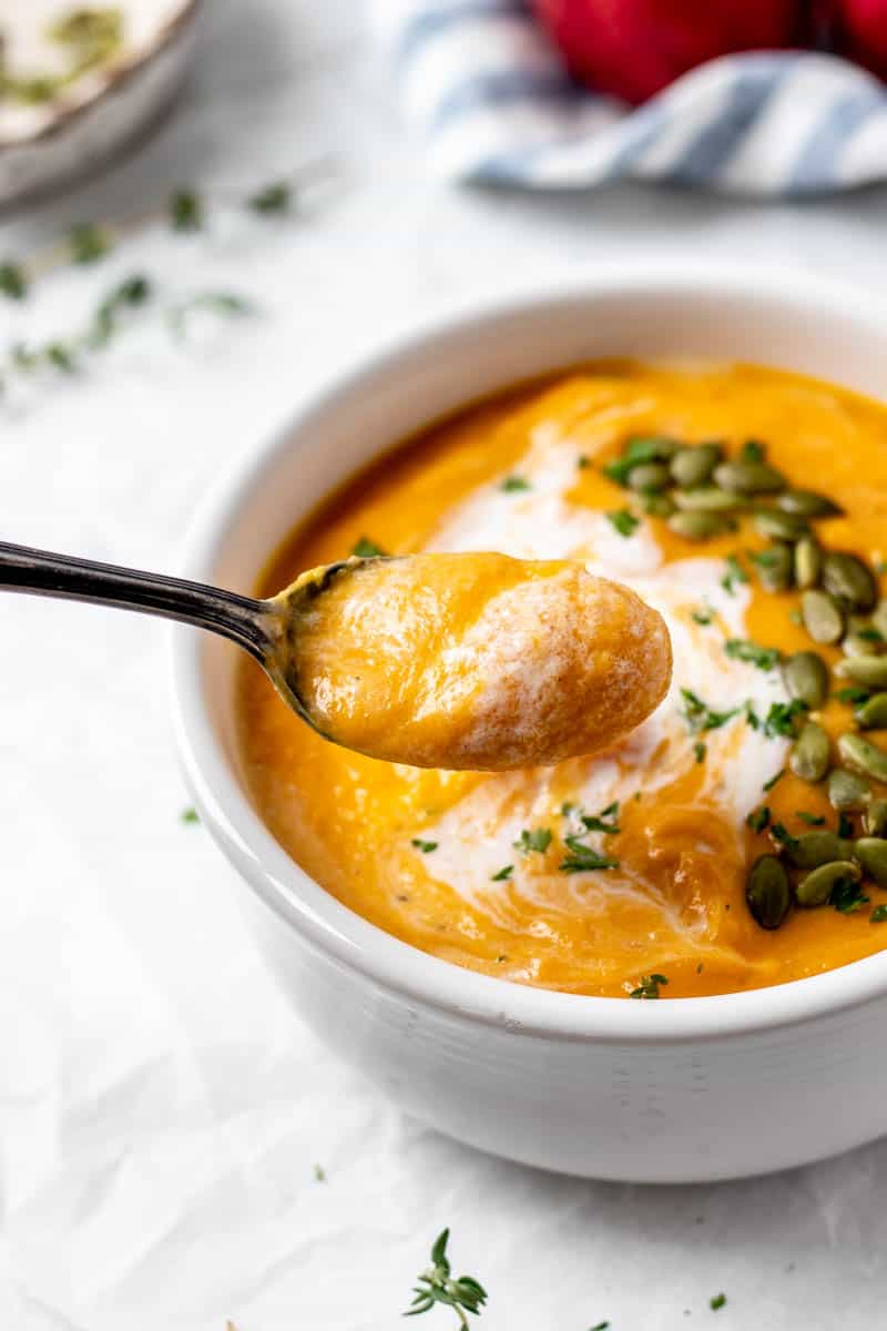 A spoon with a bite of roasted butternut squash and carrot soup.
