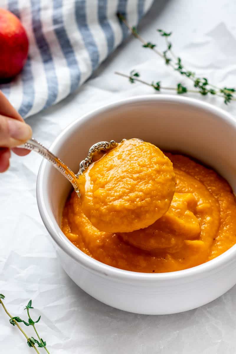 Creamy roasted butternut squash and carrot soup being ladled into a bowl.