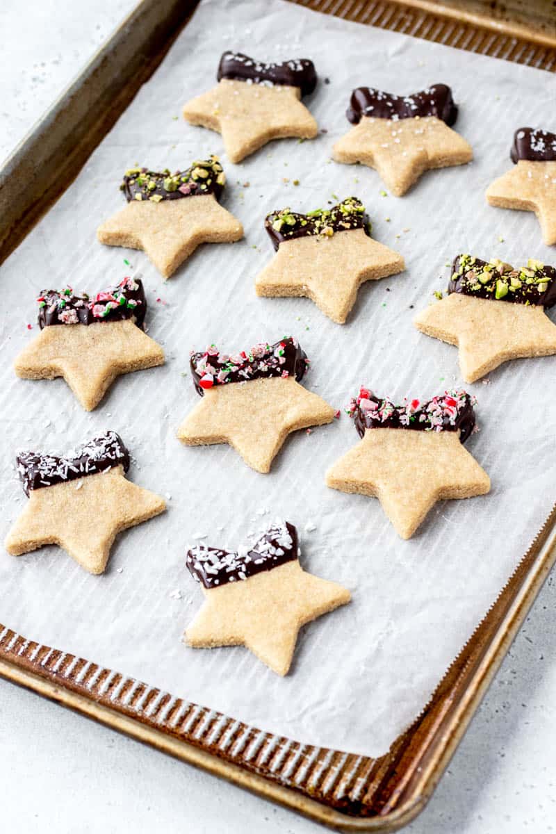 A baking sheet lined with parchment and star shaped, chocolate dipped, almond flour cookies.