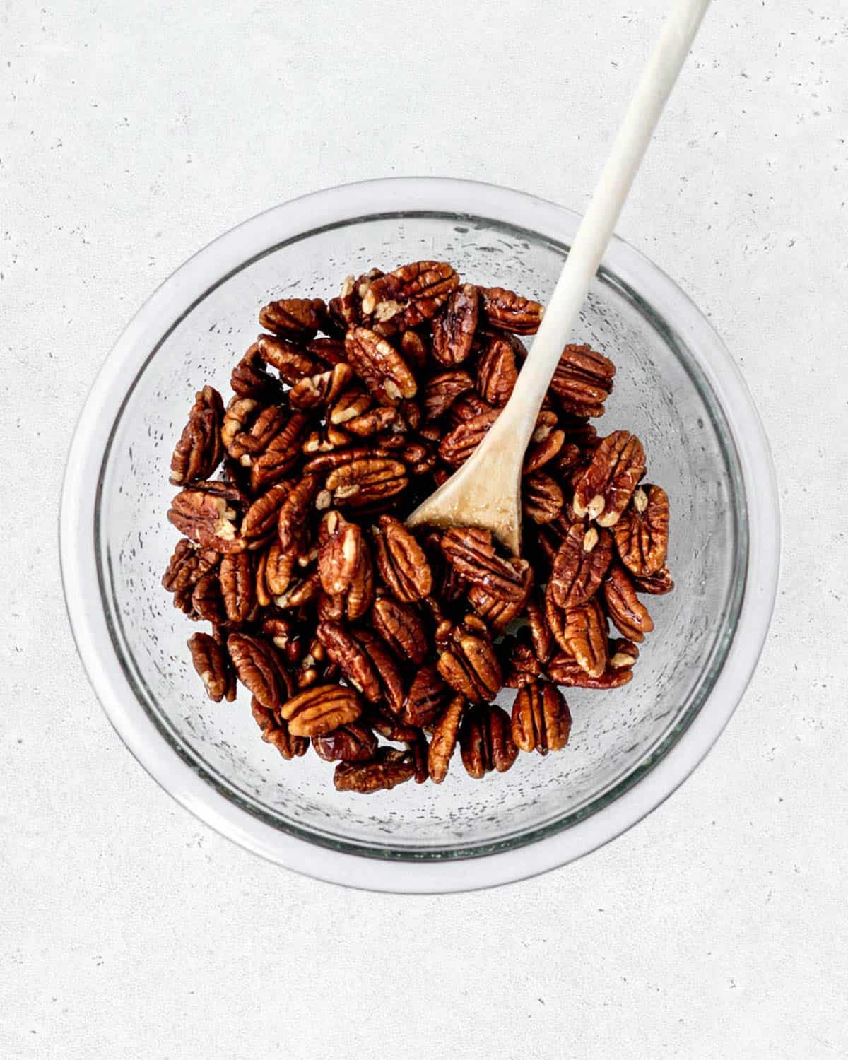 A large bowl of pecan halves mixed with maple syrup and salt.