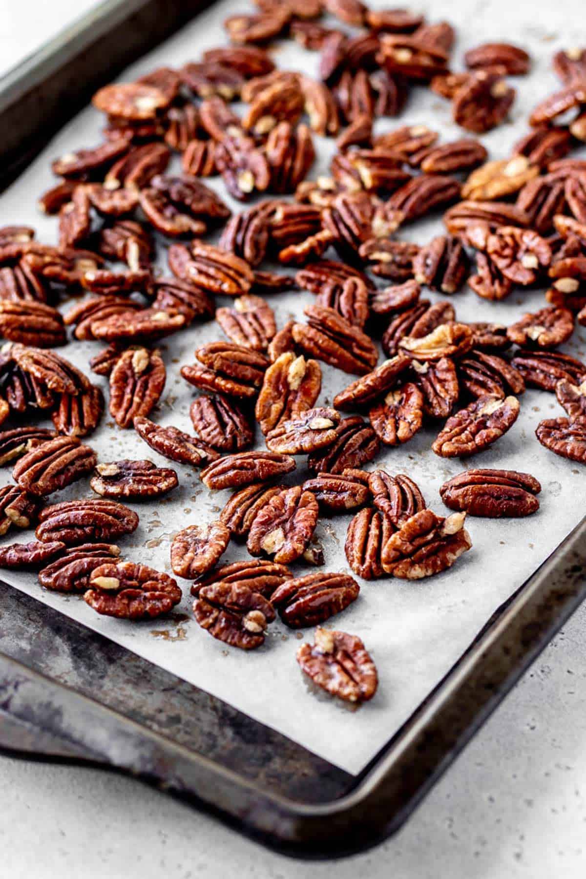 Maple syrup coated pecan halves on a parchment lined baking sheet.