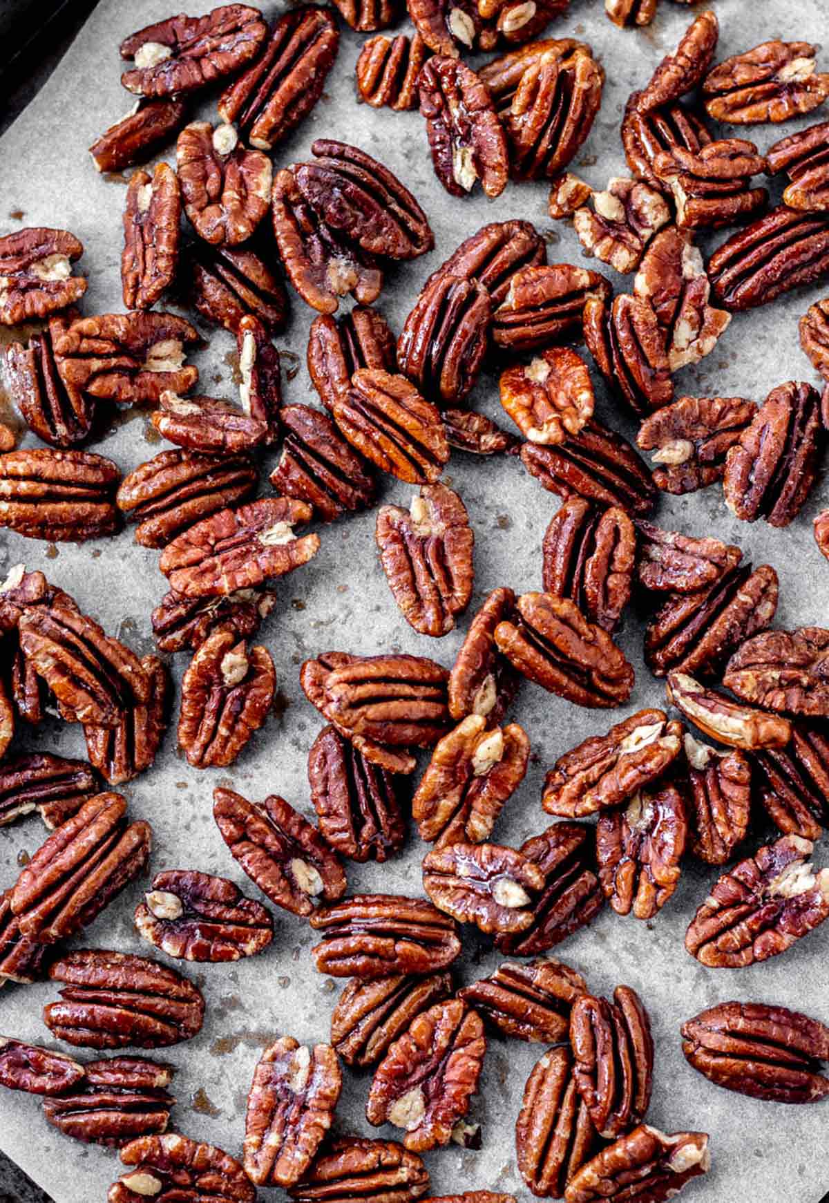A parchment lined baking sheet of maple syrup roasted pecan halves.