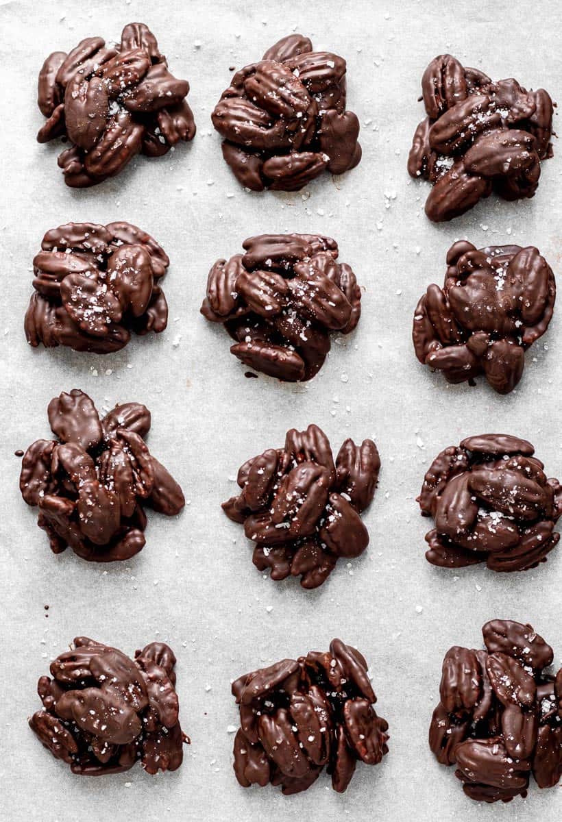 Chocolate covered pecan clusters sprinkled with sea salt on a parchment lined sheet.