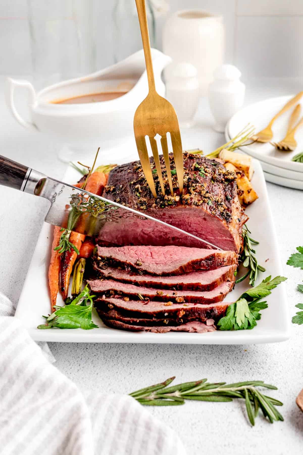 A fork holding Christmas beef roast while a sharp knife carves the roast.