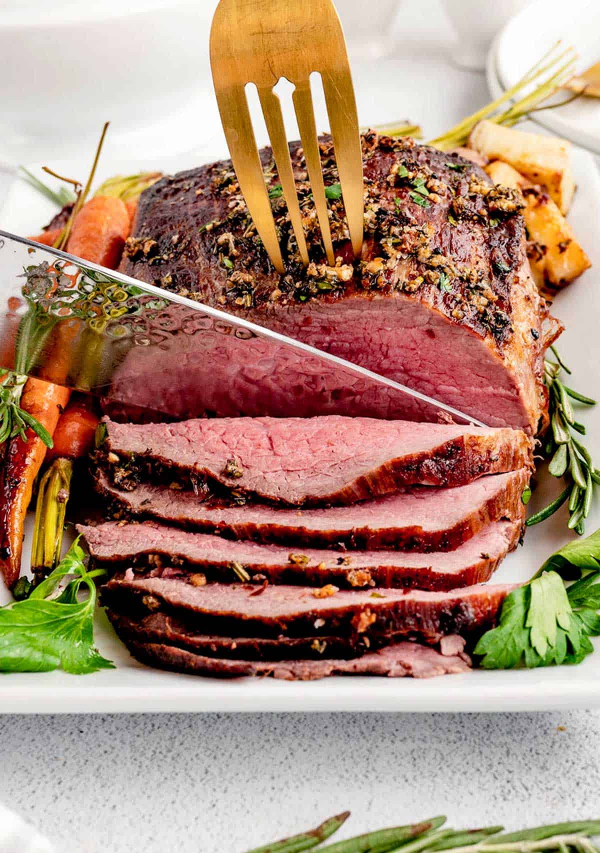 A serving fork securing the holiday roast beef, while a knife carves a slice of roast beef.