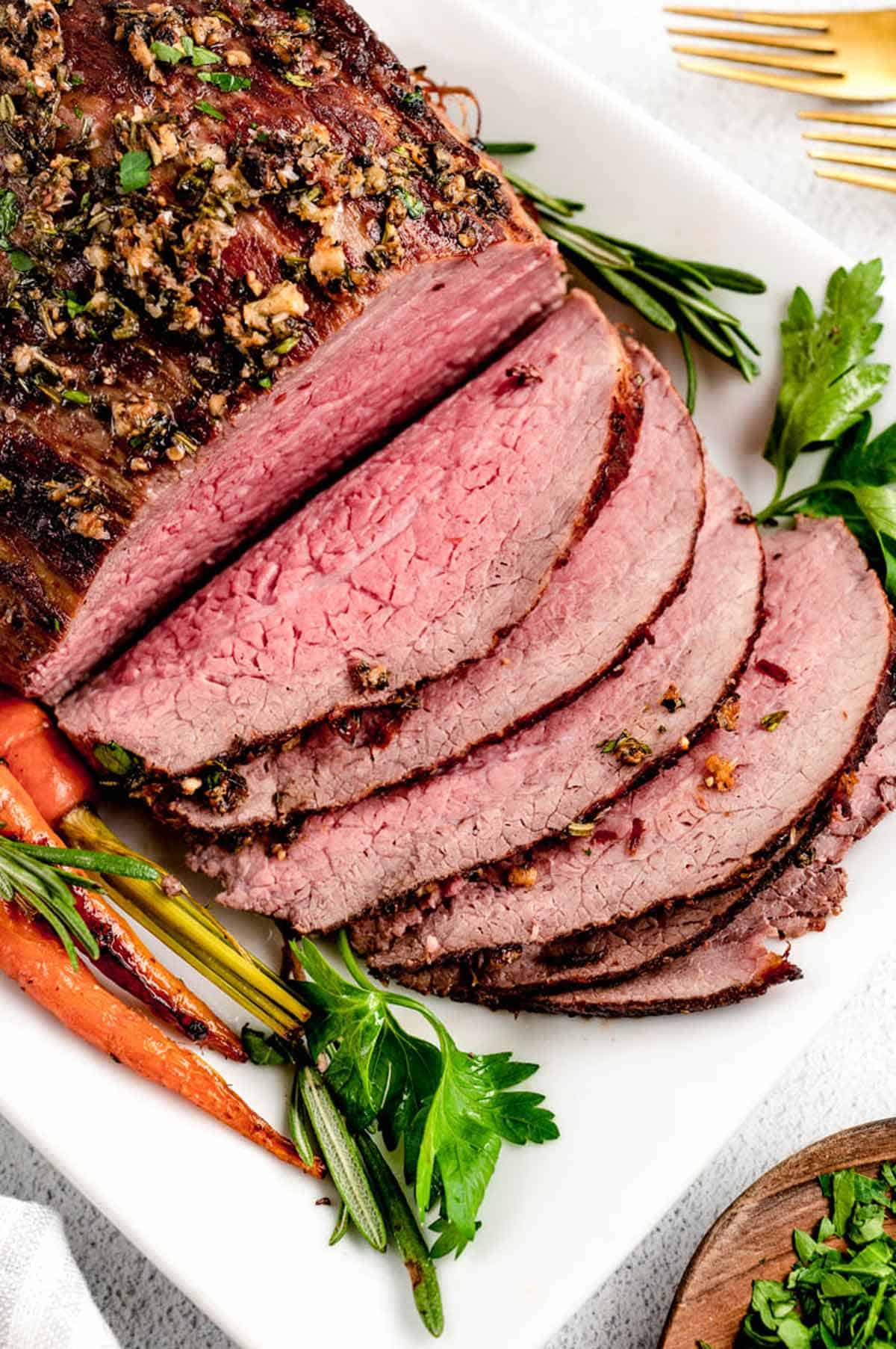 Slices cut out of a whole Christmas roast beef with roasted carrots on the side.